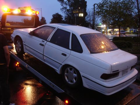 1989 Ford Taurus - White 1989 Ford Taurus loaded onto a tow truck as it begins to rain.