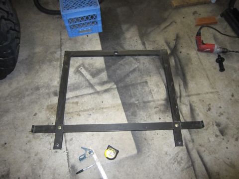 1996 Ford Bronco - A metal bracket, likely for a spare tire mount, lies on a concrete floor next to a tire and various tools.