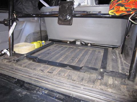 1996 Ford Bronco - The cargo area of an SUV shows a custom metal frame installed over the ribbed floor, with tie-down straps and a rolled item to the left.