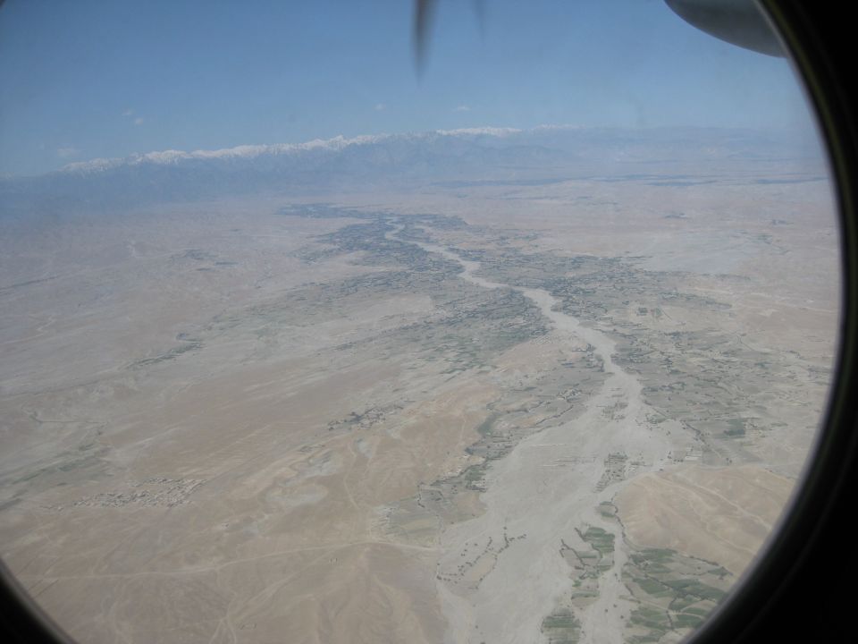 Aerial view of a river valley with snow-capped mountains in the distance, seen from an airplane window