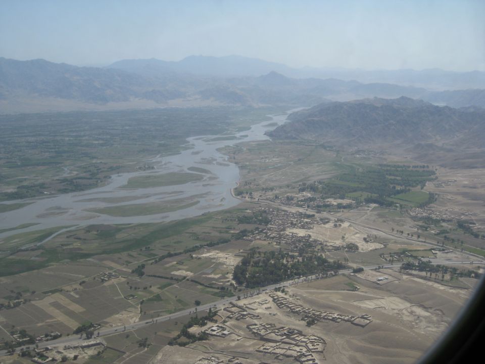 Aerial view of a wide river flowing through a valley with scattered villages and distant mountains under a hazy sky