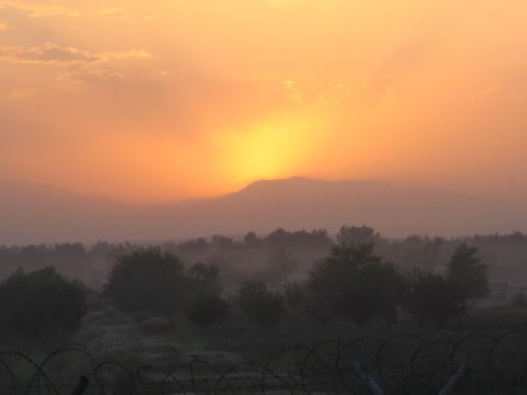 2003 Jeep Wrangler - A hazy sunset casts an orange glow over a landscape of mountains, trees, and barbed wire fencing.