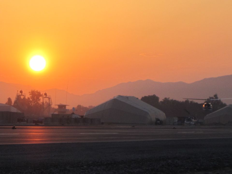 airport tarmac with hangars and mountains at sunset, helicopter in flight