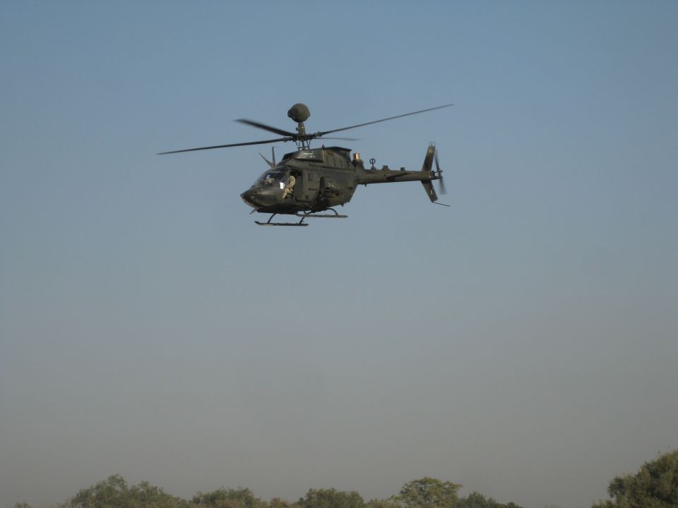 Dark military helicopter in flight against a clear blue sky