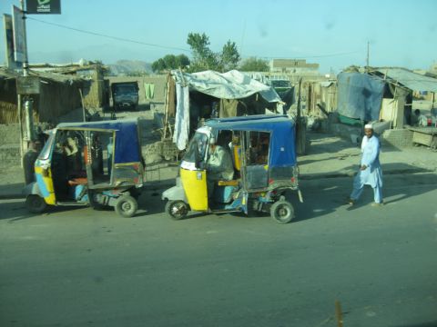 2003 Jeep Wrangler - Three-wheeled auto rickshaws are seen on a street in a dusty, built-up area.