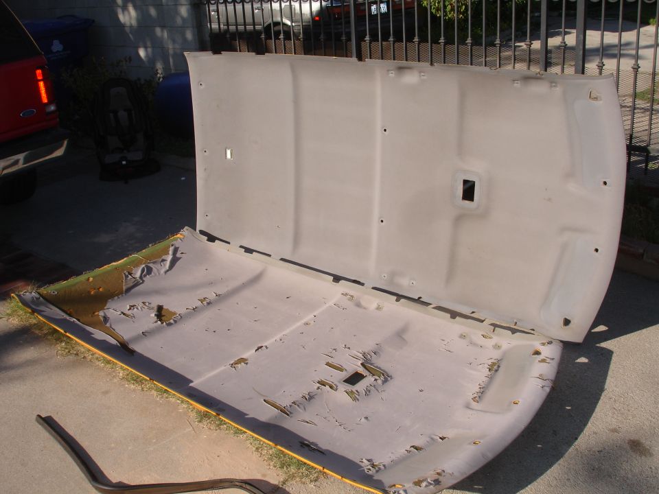 Car headliner removed from vehicle, showing damaged fabric and foam