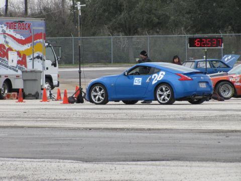 2003 Mazda Protege - A blue Nissan 370Z is parked at a race track with a timing clock in the background.