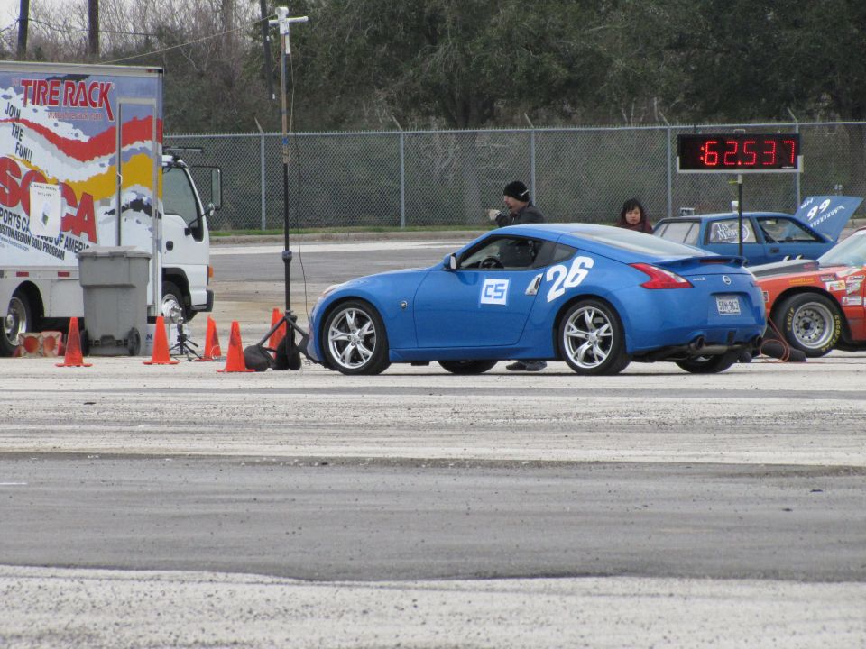 Blue sports car with number 26 on the side, parked next to a truck and other race cars