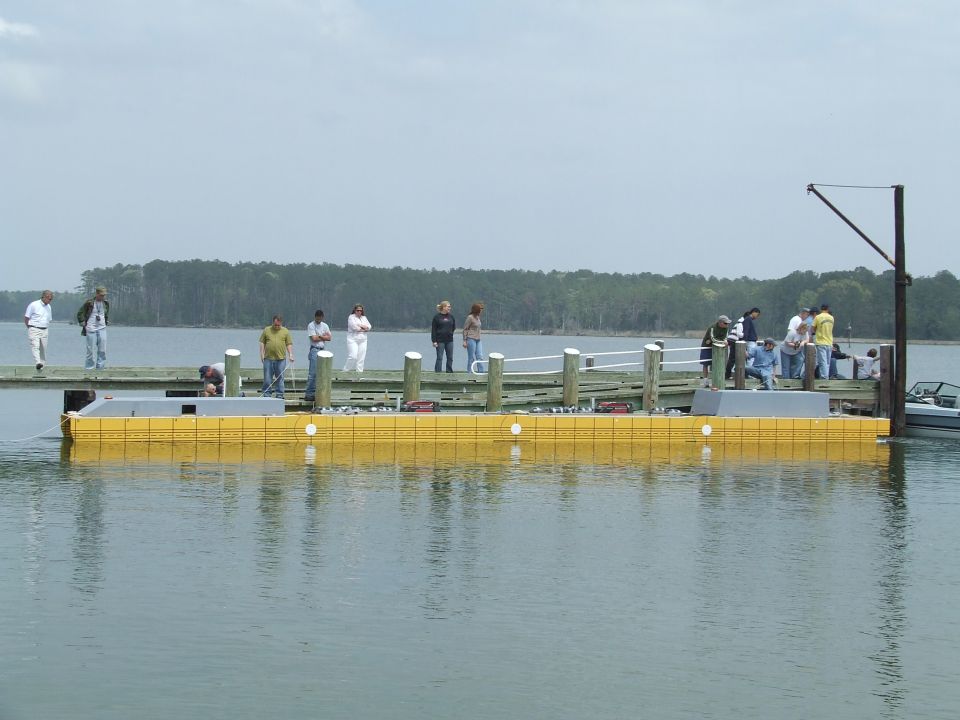 People stand on a wooden dock next to a yellow floating structure in the water
