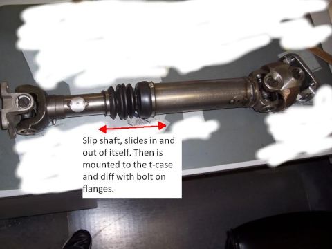 1996 Ford Bronco - A short driveshaft with a rubber slip-yoke boot and double-cardan U-joint at one end laid on a dark workbench, with white paint-over maskin…