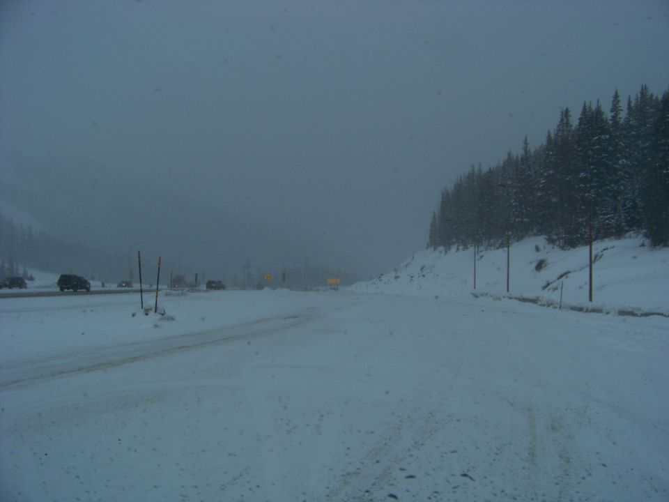 Snowy mountain road with several vehicles driving in low visibility conditions