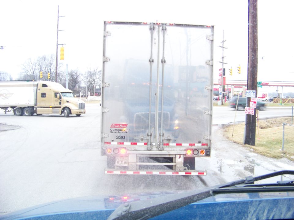 Back of a semi-truck trailer, with another semi-truck visible to the left
