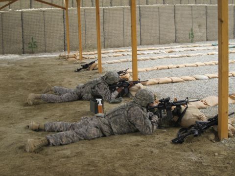2003 Jeep Wrangler - Two soldiers are seen lying prone on a sandy surface, aiming their rifles downrange at a firing range.