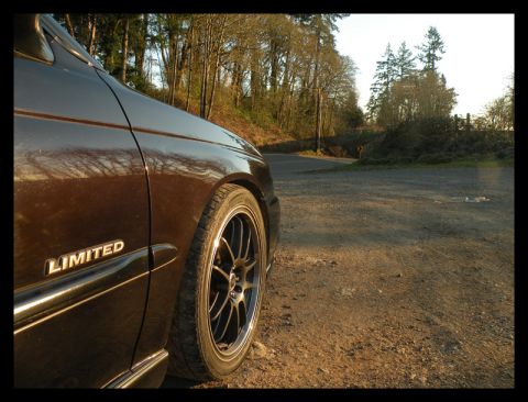 1998 Subaru Legacy - A 1998 Subaru Legacy Limited sedan is seen from the front quarter panel, parked on a dirt road with trees in the background.