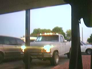 1985 Ford F-150 - A white pickup truck is viewed from the front, with another vehicle to its left and a white car behind it.