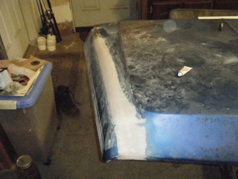 1978 Ford Bronco - A car hood is being repaired with body filler along the edge, and a tube of sealant rests on the surface.