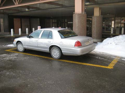 1999 Ford Crown Victoria - A silver sedan, possibly a police or traffic vehicle, is parked in a designated spot near a building entrance.