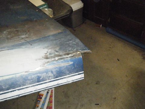 1978 Ford Bronco - A close-up of a damaged blue car door with a white stripe, revealing rust and metalwork in need of repair.