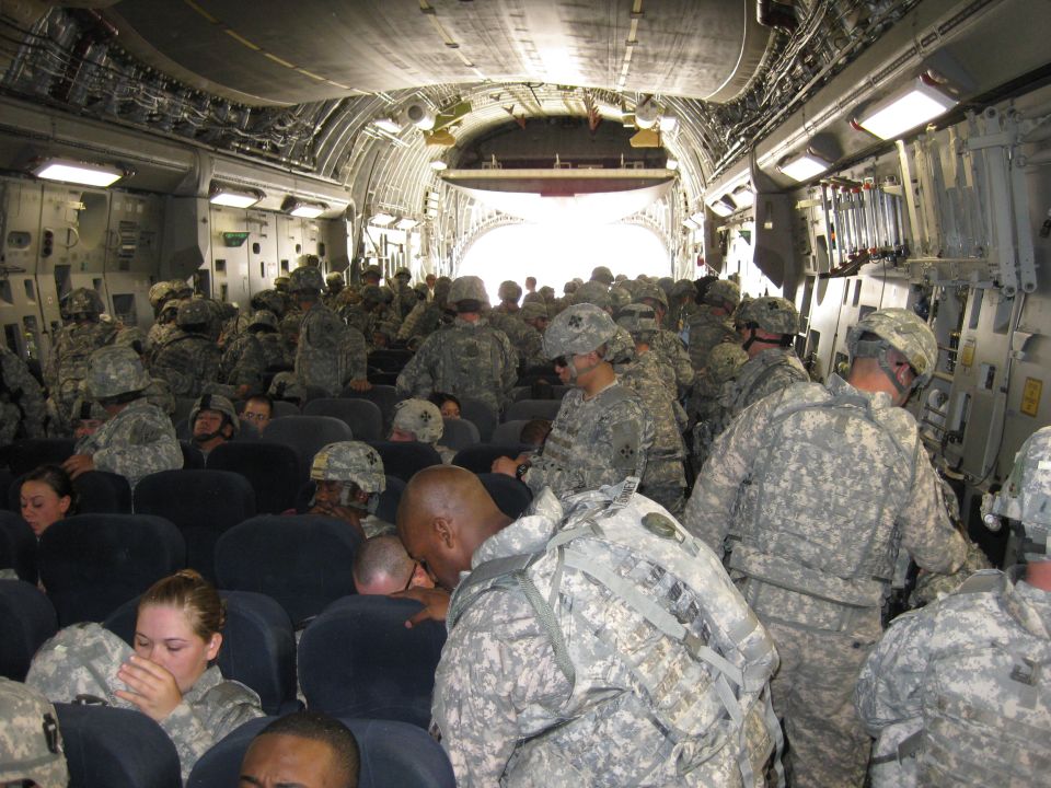 Soldiers in camouflage uniforms sitting in rows inside a cargo plane