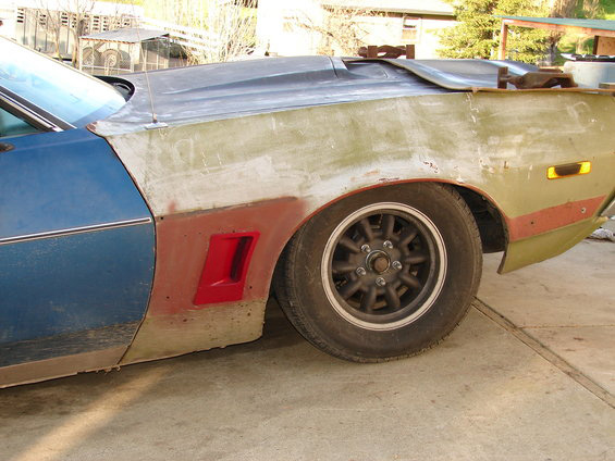 Side view of a car fender being prepped for paint, showing a red vent and a multi-spoke wheel