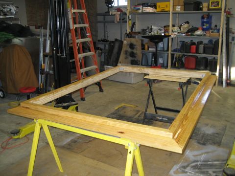 1996 Ford Bronco - Wooden frame assembly supported by yellow sawhorses in a garage with shelves and tools in the background.
