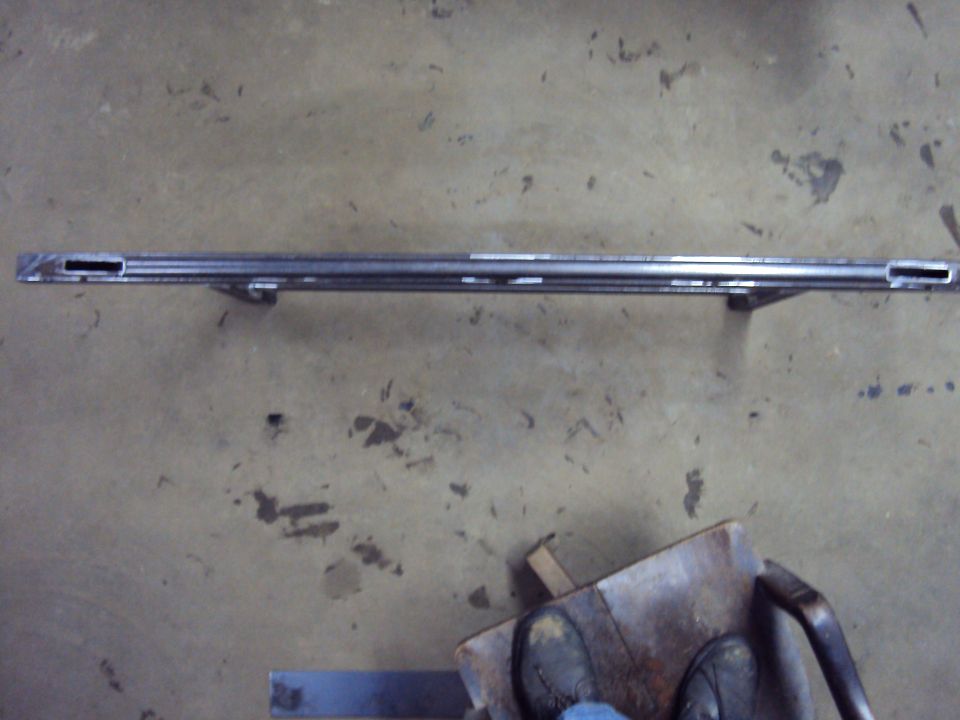 Bare metal crossmember bar with slotted ends and welded brackets on a concrete garage floor