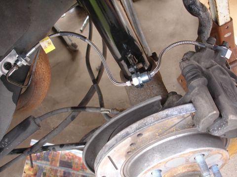 1995 Ford Taurus - Close-up view of a rear brake caliper, rotor, and stainless steel brake lines.