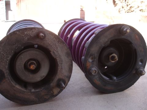 1995 Ford Taurus - A close-up view of two automotive suspension struts, one a vibrant purple coil spring.