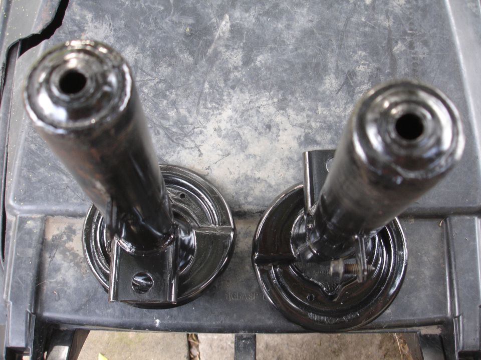Two black painted suspension parts, possibly strut mounts or similar components, resting on a dark surface