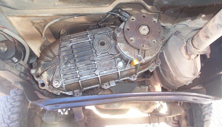 Underside view of a transfer case and rear driveshaft yoke on a truck, viewed from below