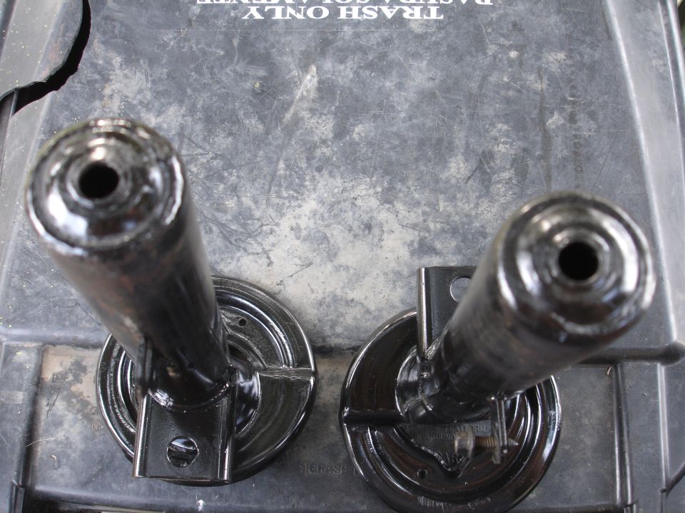 Two black suspension components with circular bases on a textured surface with text