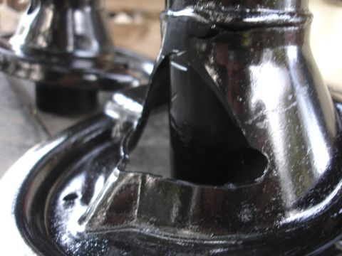 1995 Ford Taurus - Close-up of a damaged black metal automotive component, showing a triangular opening and stress fractures.