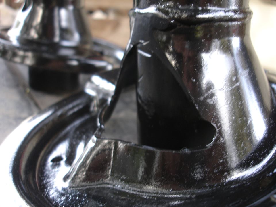 Black metal automotive part with a triangular cutout and visible cracks