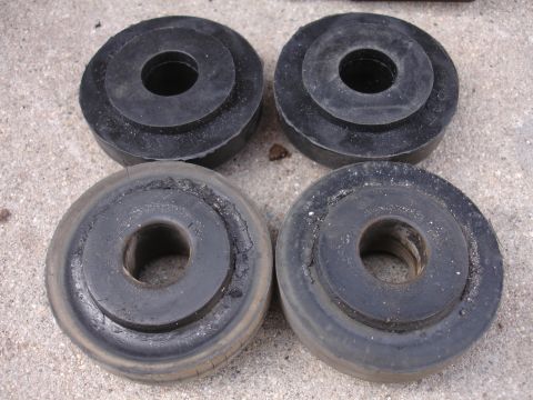 1995 Ford Taurus - Four black rubber suspension bushings are shown, with two appearing new and two exhibiting signs of wear and cracking.