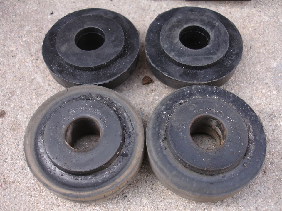 Four black rubber suspension bushings, two appear new, two show wear