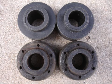 1995 Ford Taurus - A set of four suspension bushings, two made of rubber and two of metal with visible bolt holes, are displayed on a concrete surface.