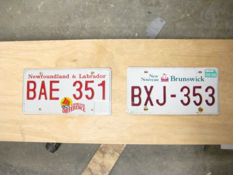 1999 Ford Crown Victoria - Two license plates are displayed on a wooden surface, one from Newfoundland & Labrador and the other from New Brunswick.