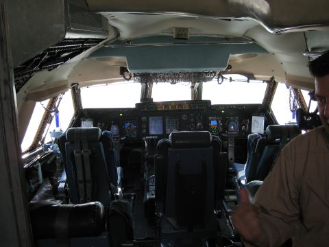 2003 Jeep Wrangler - Interior of a large military transport aircraft flight deck, looking forward past empty crew seats with five-point harnesses toward a glass…
