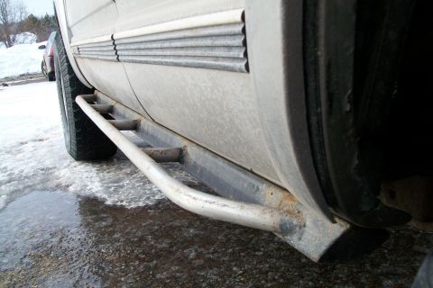 2000 Chevrolet Tahoe - The side of a dirty 2000 Chevrolet Tahoe with aftermarket side step bars is shown in this close-up, with a second vehicle visible in the ba…