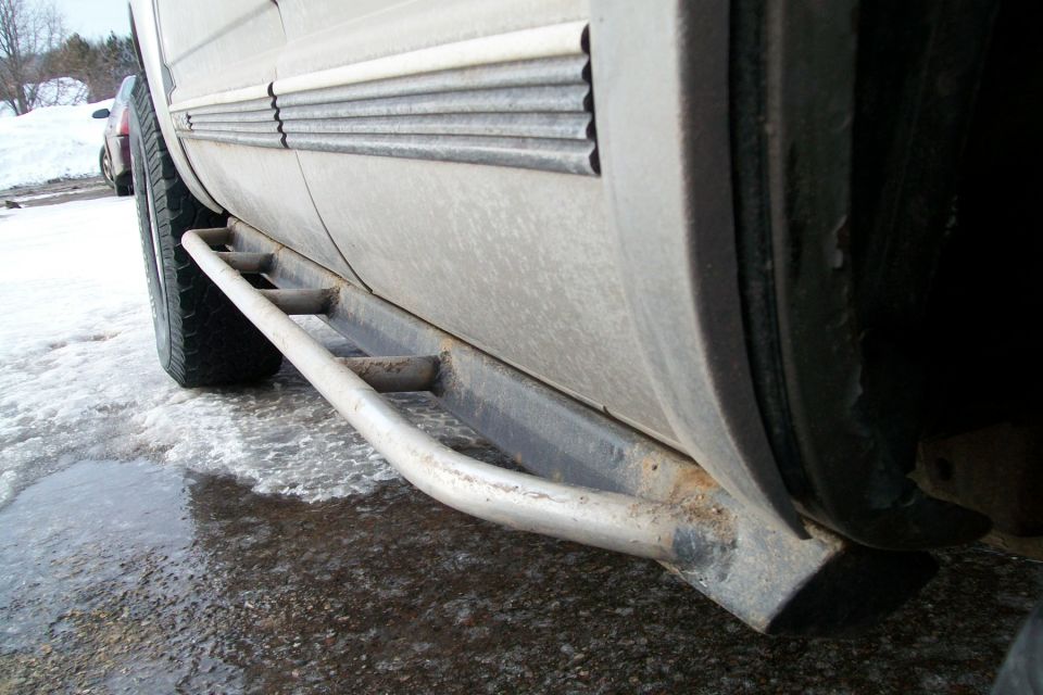 2000 Chevrolet Tahoe side step bars, dirty white body, rusty metal, tire visible