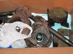 1990 Ford Bronco - A cardboard box packed with disassembled front axle parts — rusty inner and outer axle shafts, a spindle, knuckle castings and a cast housi…