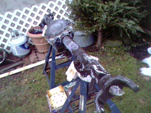 1990 Ford Bronco - A greasy solid front axle housing resting across a folding metal work stand in a snow-dusted backyard, with the axle tube running to a stee…
