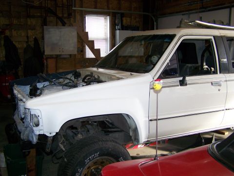 1988 Suzuki Samurai - A white SUV, possibly a Toyota 4Runner, is shown in a garage with its hood removed, revealing the engine bay. Another vehicle is parked in…