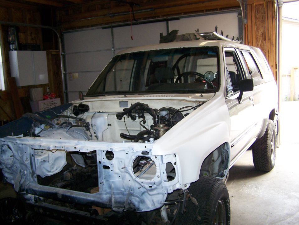White SUV with front end disassembled for repair, showing engine bay and interior