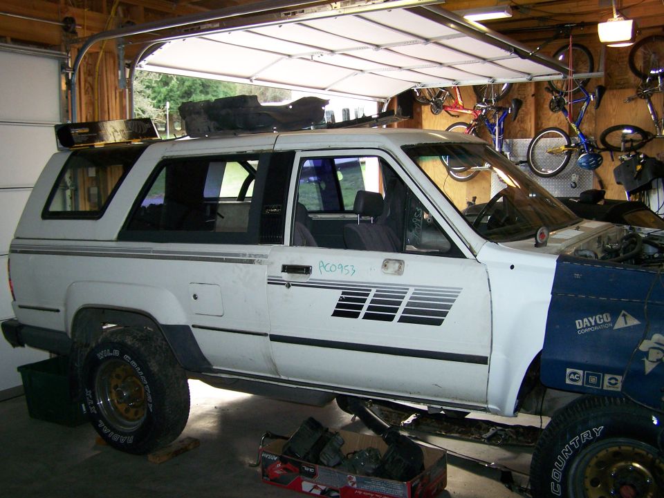 White SUV with a blue front end, undergoing repairs in a garage