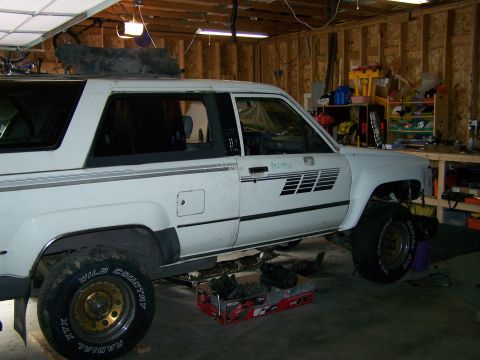 1988 Suzuki Samurai - White SUV in a garage, appearing to be undergoing repairs or modifications. The vehicle has distinctive side graphics.