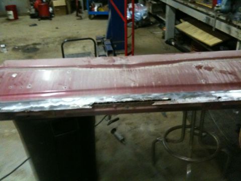 1993 Ford Bronco - A red metal panel, likely a car door or fender, is undergoing repair for rust damage with body filler visible.