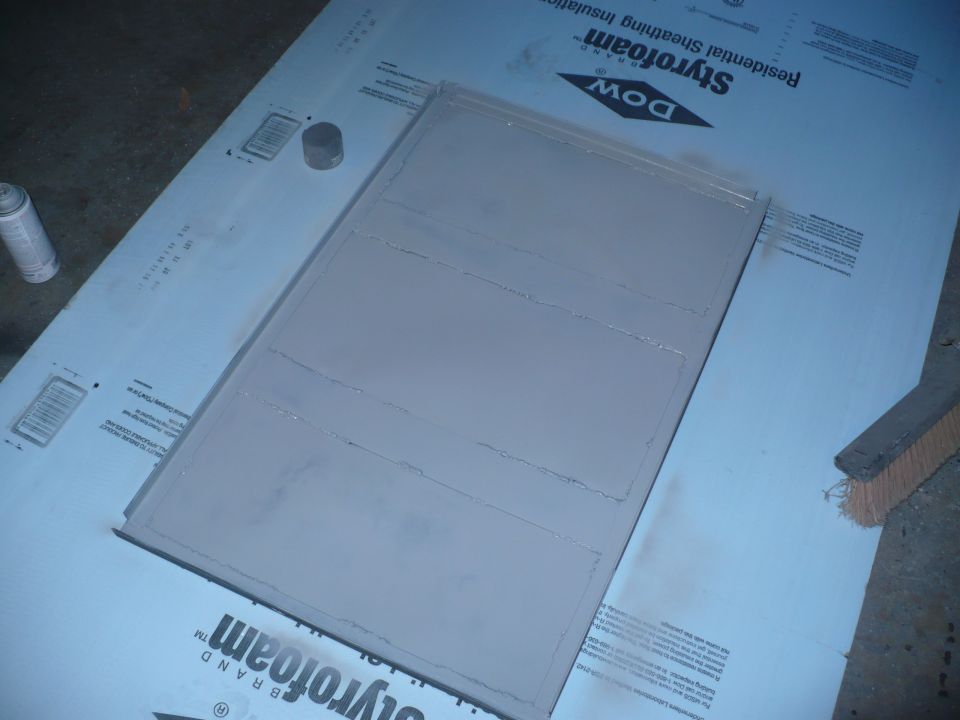 Gray painted panel with horizontal lines, sitting on Styrofoam insulation board. Spray can and brush nearby