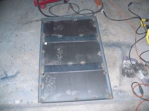 1979 Ford Bronco - A metal panel, likely a custom fabrication, sits on a concrete floor near welding tools and protective gloves.