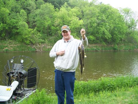 1979 Ford F-250 - A man proudly displays his catch of the day next to an airboat by the water.